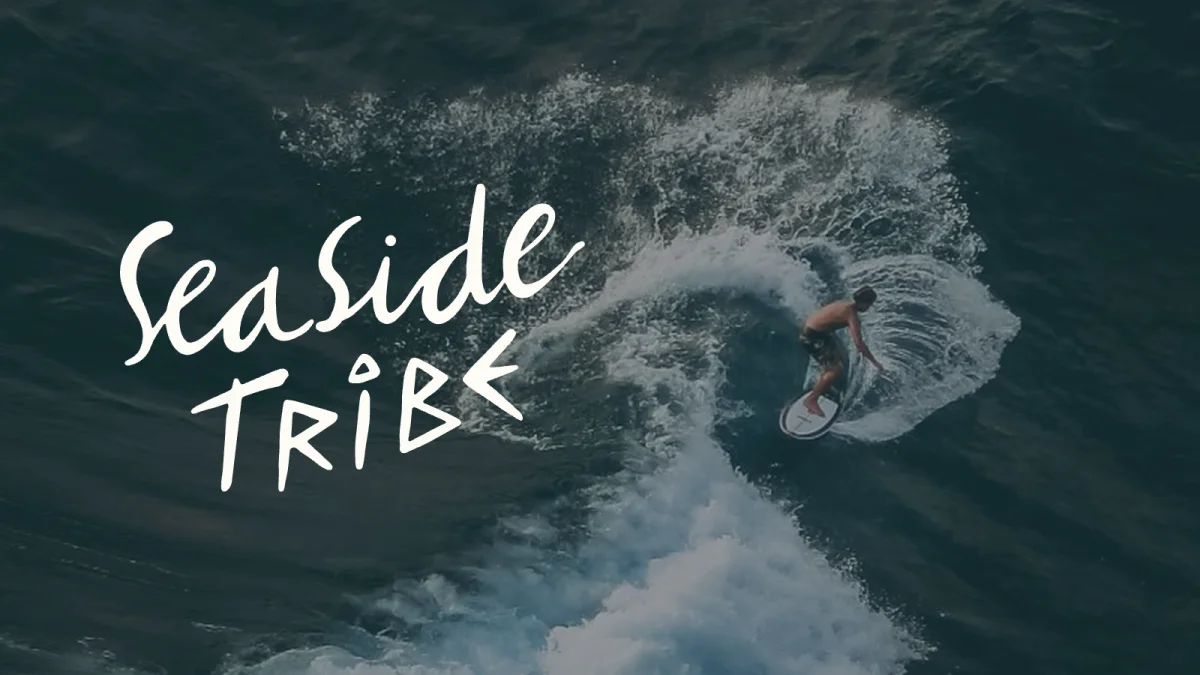 Seaside-Tribe-Wortmarke neben einem Surfer in der Welle